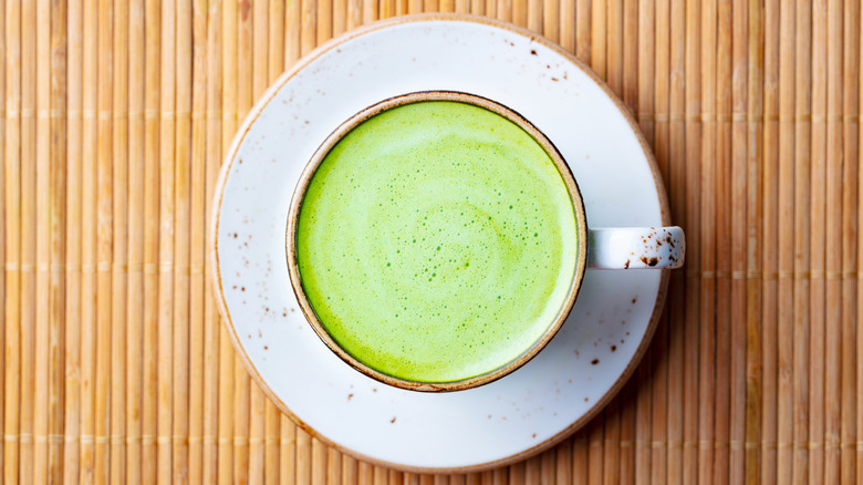 Matcha latte in a mug on a rustic white place on top of bamboo.