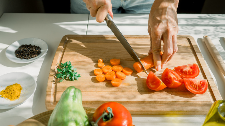 Two hands cut a carrot on a sun-dappled cutting board