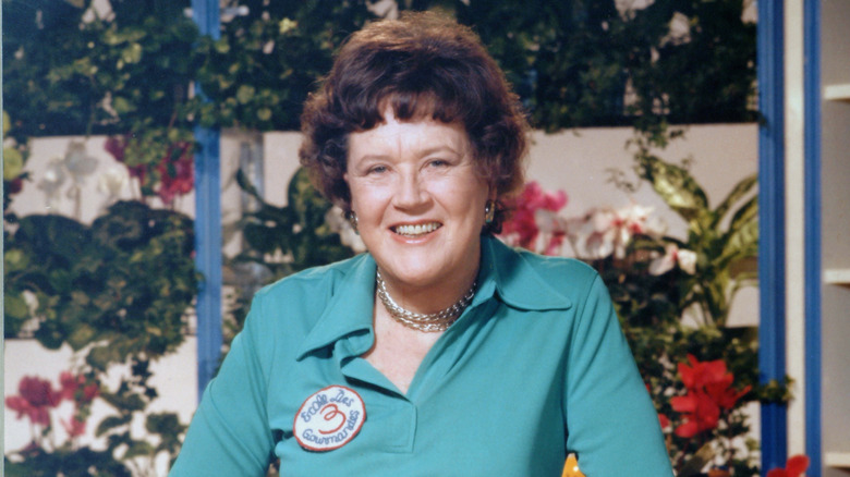 Julia Child wearing a turquoise top in front of a floral background