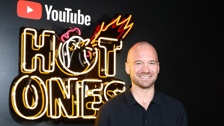 Sean Evans smiling in front of a Hot Ones sign with the YouTube logo.