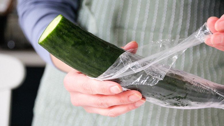 Person holding chopped cucumber and pulling back its plastic wrap.