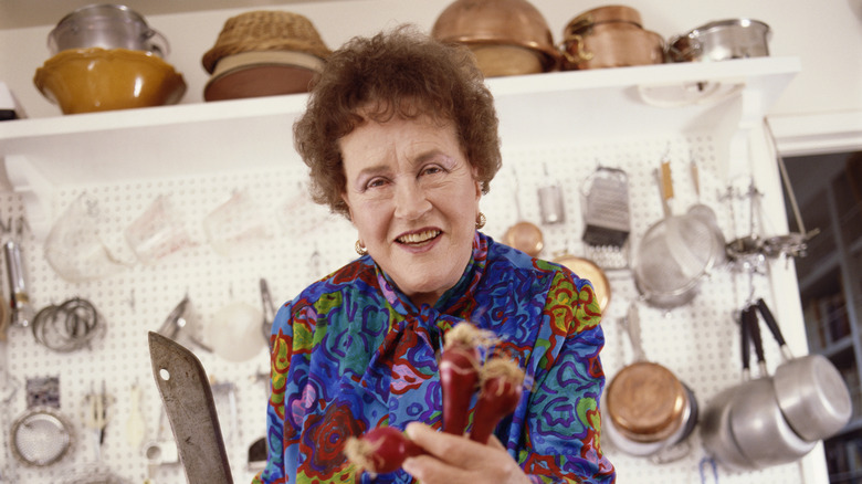 Julia Child in a kitchen holding a knife and vegetables