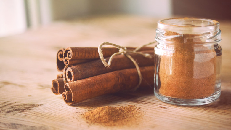 Jar of ground cinnamon next to cinnamon sticks