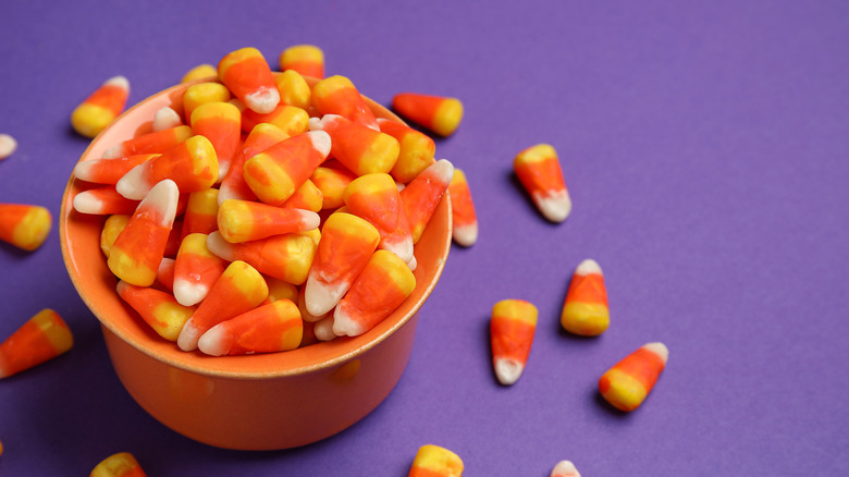 Candy corn in a wbowl on a purple background.