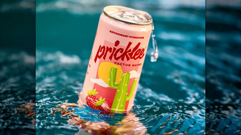 Someone holds a can of Pricklee cactus water in Strawberry Hibiscus flavor in a pool as water drips off of the can