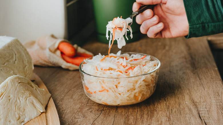 Man eating a forkful of fermented sauerkraut on a wooden countertop