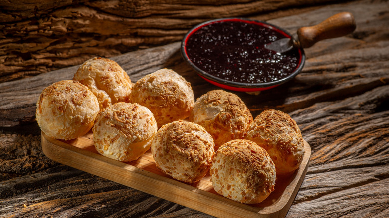 Pão de queijo on a wooden tray placed on a wooden table with a spread in the background
