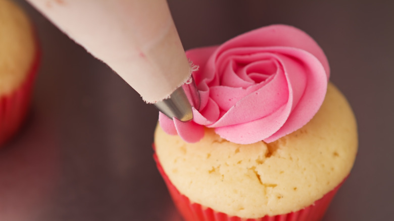 Piping a pink rose on a cupcake