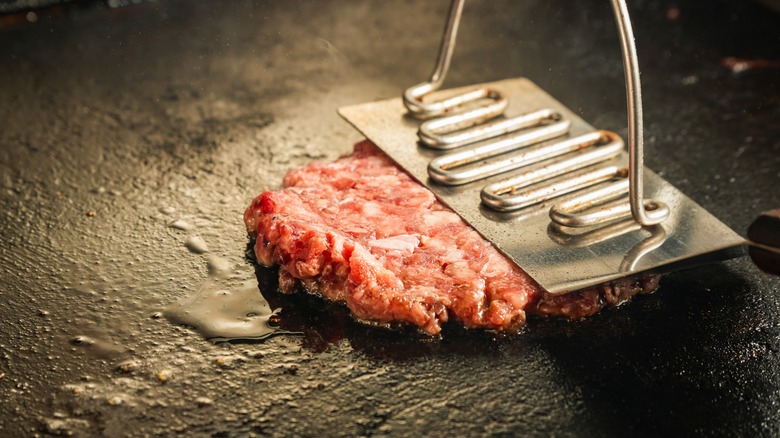 Smashing a hamburger patty on a hot surface