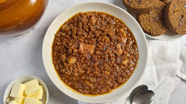 bowl with baked beans and two spoons next to cubed butter and bread