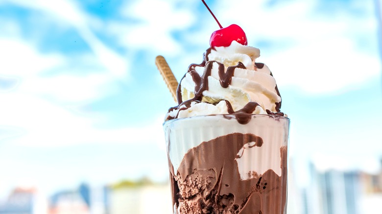 Chocolate milkshake with whipped cream and a cherry against a sky background
