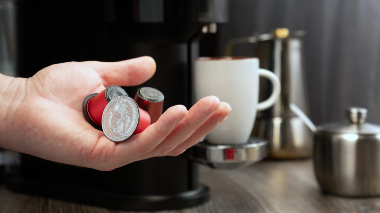 Hand holding coffee pods in front of coffee machine