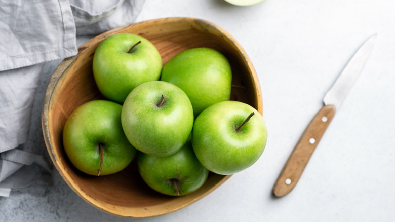Bowl of green Granny Smith apples on a white background with a knife