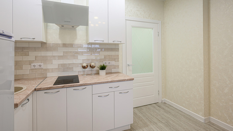 Modern, bright kitchen with white cabinets, a neutral backsplash, and light wood flooring