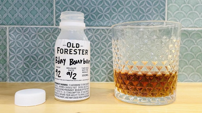 Open Sample bottle and rocks glass of Old Forester Birthday Bourbon 2025 with