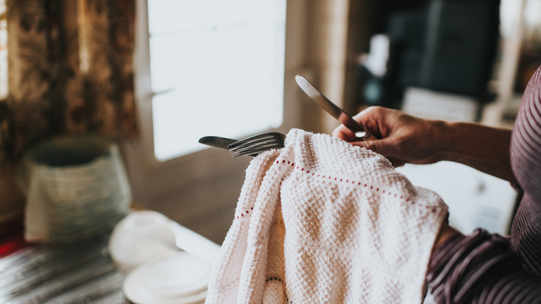 Person drying cutlery with a towel.