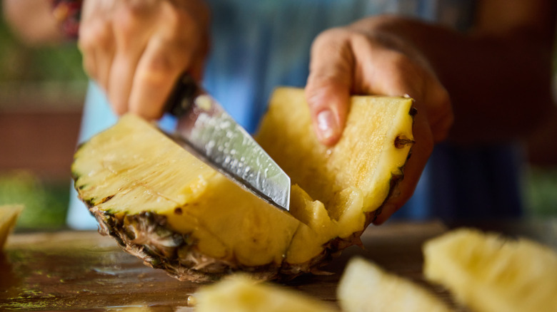 Hand slicing fresh pineapple with a knife.