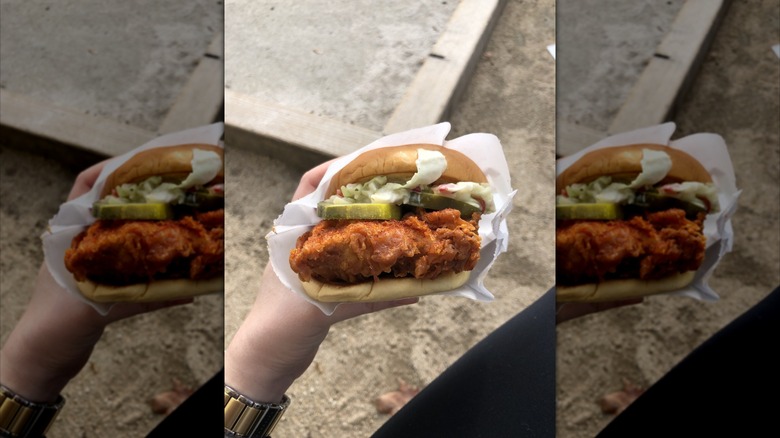 Someone holds a Shake Shack crispy chicken sandwich, with pickles and lettuce visible