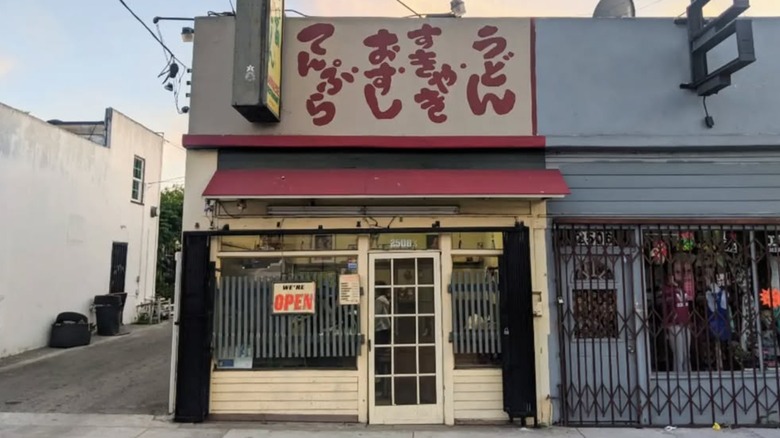 The exterior of Otomisan restuarant, a small beige building with red signs and a red awning