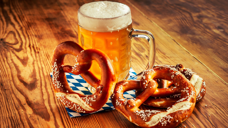 Three salted pretzels near a full beer mug with foam on top