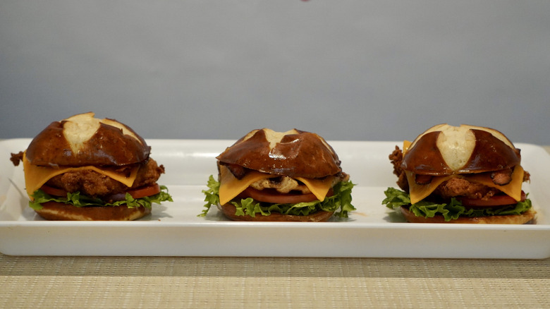 Pretzel Cheddar Club Sandwches on a white plate placed on a tan table in front of a white Chick-fil-A step and repeat