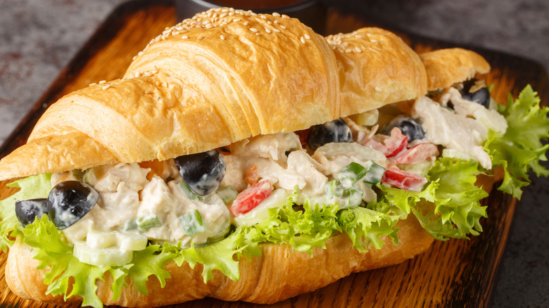Chicken salad on a croissant with lettuce on a wooden cutting board