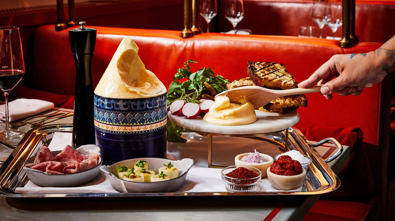 Closeup of Butter Service Garni on a white plate, with a hand spreading butter on a piece of bread using a wooden spatula