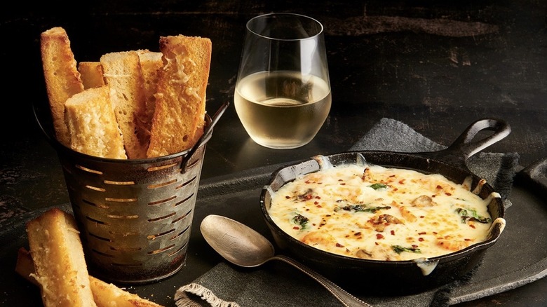 Skillet filled with cheesy Seafood Fondeaux served with bread and a glass of white wine
