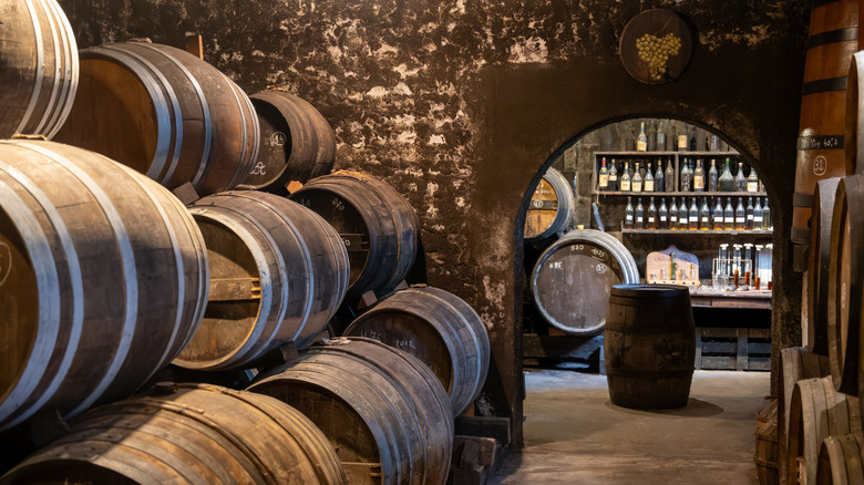 Wine aging in stacks of old barrels with a view of more barrels and bottles through an archway