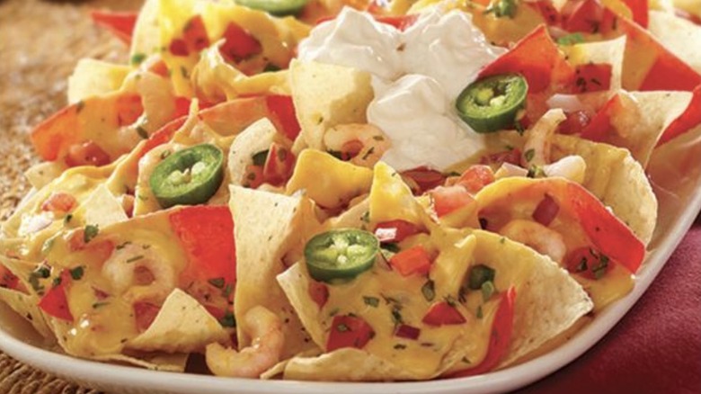 Shrimp, jalapeños, pico de gallo, sour cream, and melted cheese atop a plate of tortilla chips
