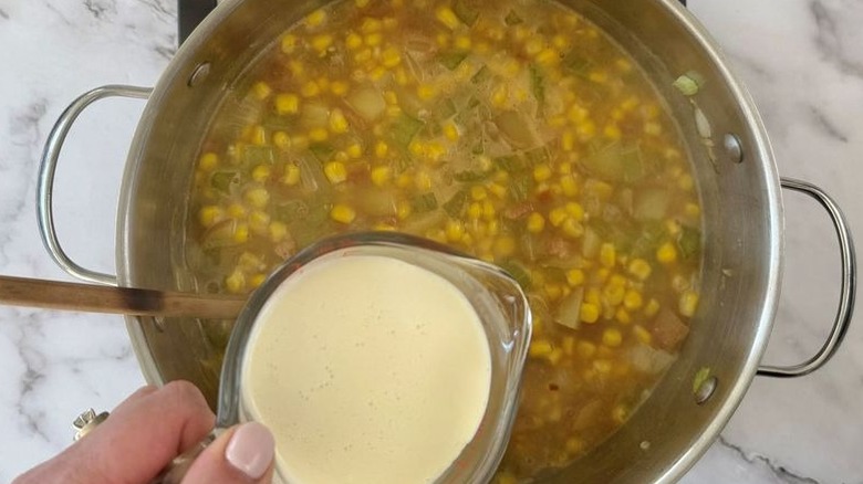 Measuring cup full of cream above large soup pot