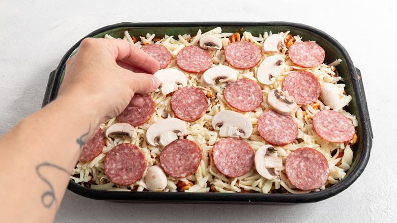 adding pepperoni and mushrooms to pasta bake