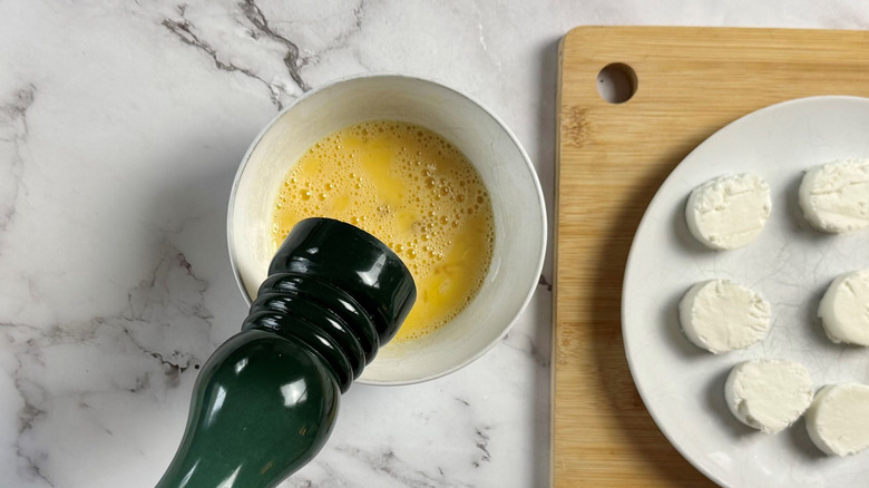 Pepper grinder over bowl with beaten egg