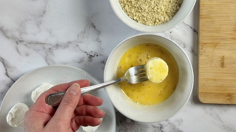 Fork holding goat cheese slice in egg wash