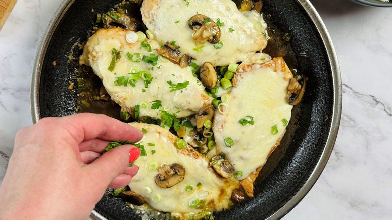hand sprinkling parsley on top of baked chicken in pan