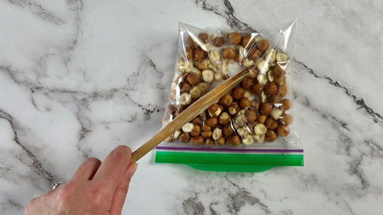Wooden spoon pressing on hazelnuts in plastic baggie