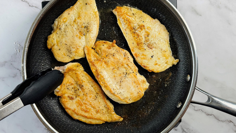 Four pieces of browned chicken breasts in frying pan