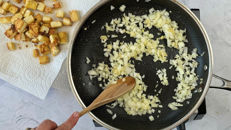 hand stirring onions in pan