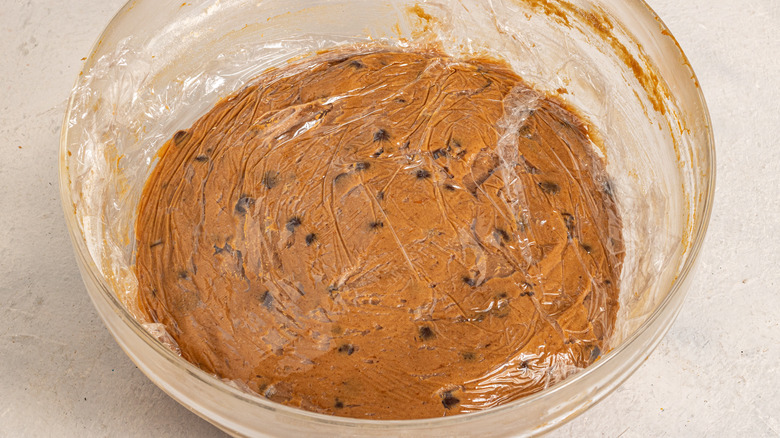Bowl with cookie batter and a plastic wrap on top.