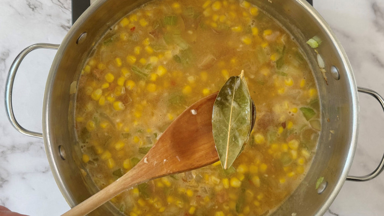 Wooden spoon removing bay leaf from soup
