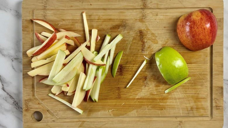 Red and green apple sliced into matchsticks on cutting board