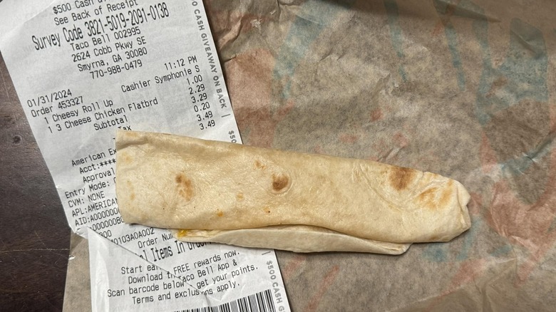 A Taco Bell Cheesy Roll Up sits on top of both a receipt and its wrapper