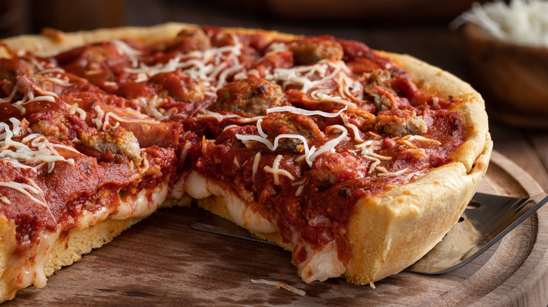 A deep dish Chicago style sausage pizza has a piece cut out