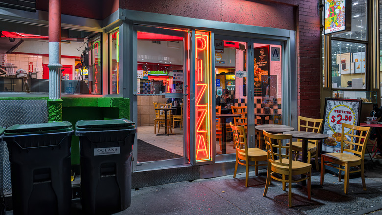 The exterior of a NYC pizza parlor glows with neon lights