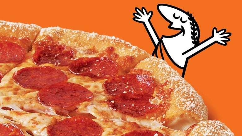 The Little Caesars cartoon mascot stands with his arms raised triumphantly over a pepperoni pizza