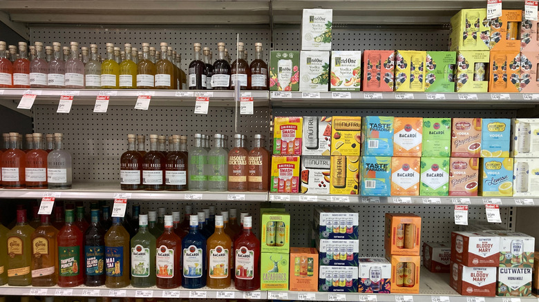 A variety of different alcoholic beverages sit on a shelf in a supermarket
