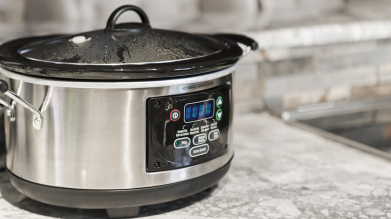 A slow cooker sits on a countertop with condensation on the inside of the lid