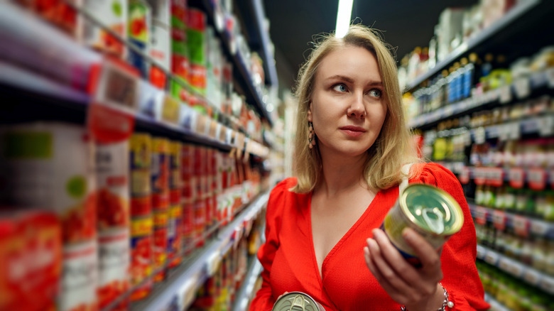 Woman choosing canned tomatoes at grocery store
