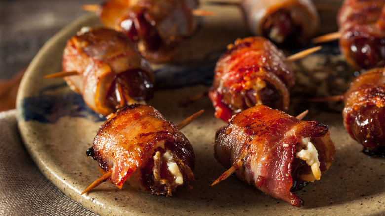 Bacon-wrapped dates stuffed with cheese sit on a plate.