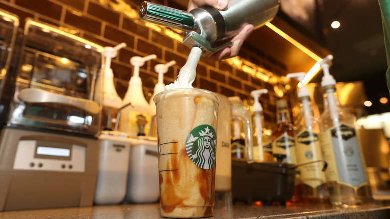 Starbucks barista adding foam to a drink in front of syrups